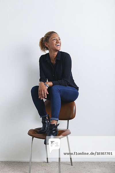 Porträt einer lächelnden Frau auf der Rückenlehne eines Stuhls vor weißem Hintergrund