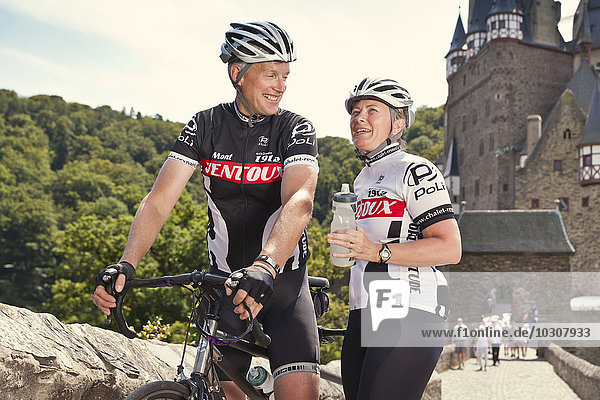 Germany  Rhineland-Palatinate  US American couple standing in front of Eltz Castle with their tandem