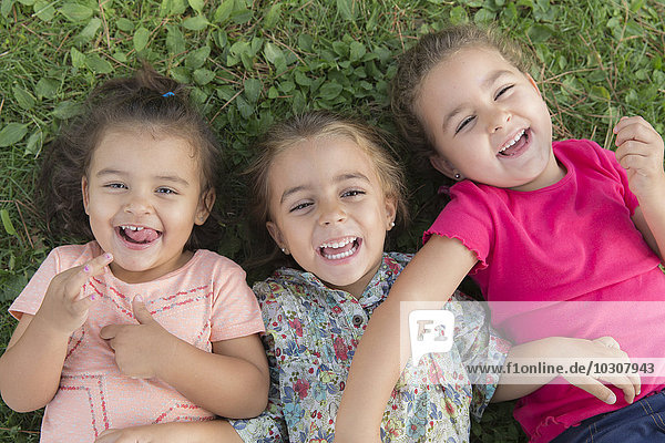 Porträt von drei lachenden kleinen Mädchen  die nebeneinander auf einer Wiese liegen.