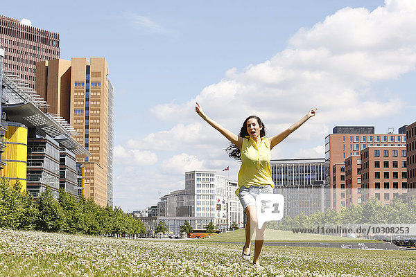 Deutschland  Berlin  fröhliche junge Frau tanzt auf einer Wiese am Potsdamer Platz