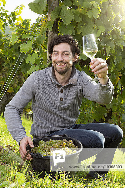 Deutschland Bayern Volkach glücklicher Winzer im Weinberg mit einem Glas Weißwein