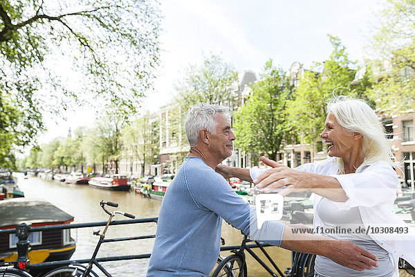 Netherlands  Amsterdam  exuberant senior couple embracing at town canal