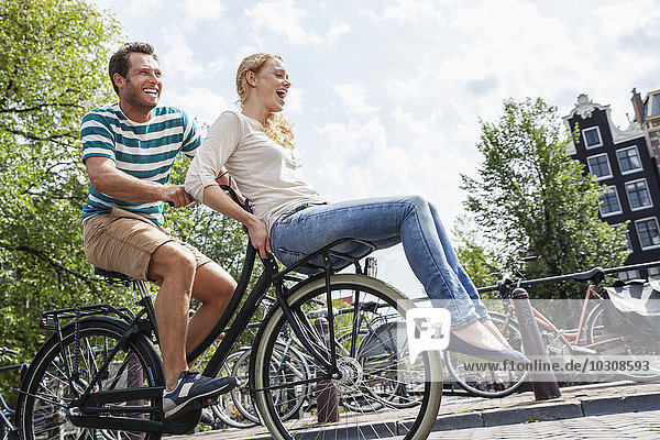 Niederlande  Amsterdam  glückliches Paar beim Fahrradfahren in der Stadt