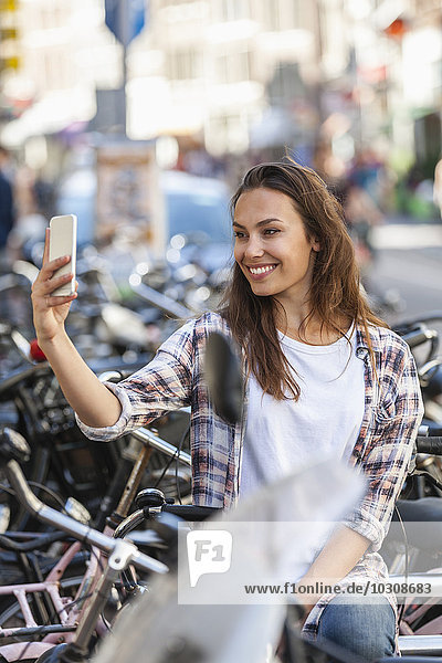 Niederlande  Amsterdam  lächelnde junge Frau mit einem Selfie