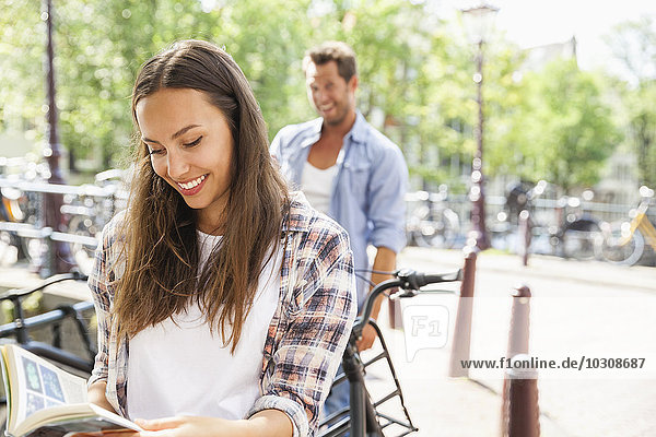 Netherlands  Amsterdam  smiling young woman reading book with man in background
