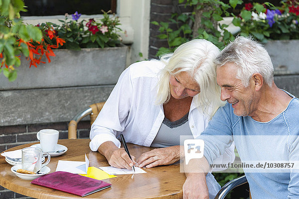 Seniorenpaar beim Schreiben von Postkarten im Outdoor-Café