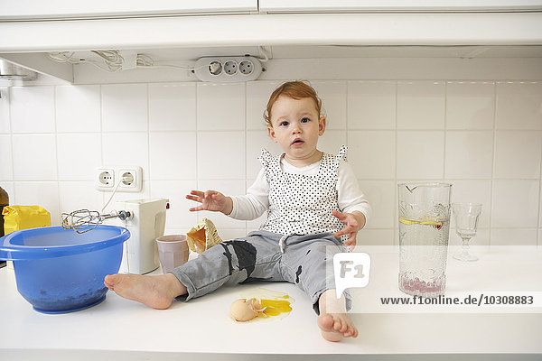Kleines Mädchen sitzt auf der Küchentheke mit zerbrochenem Ei