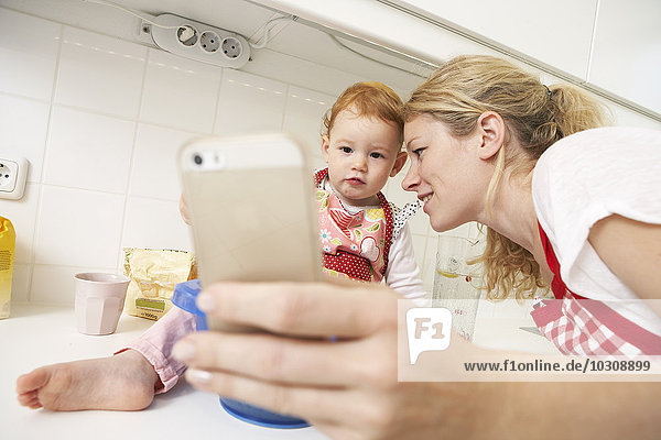 Junge Frau  die einen Selfie mit ihrer kleinen Tochter in die Küche nimmt