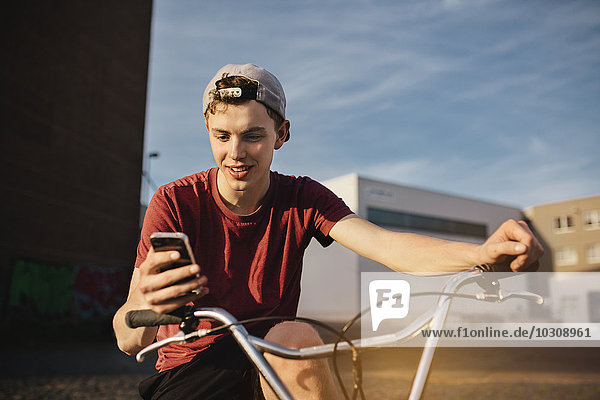 Junger Mann mit BMX-Fahrrad sucht auf dem Handy