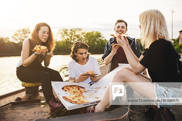 Freunde sitzen zusammen im Freien und teilen sich eine Pizza.