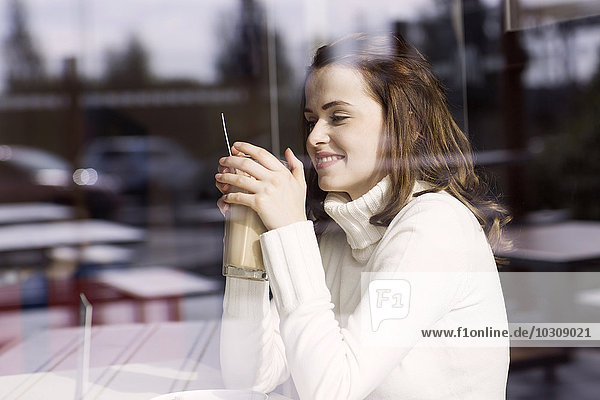 Smiling young woman with Latte Macchiato sitting in a cafe looking