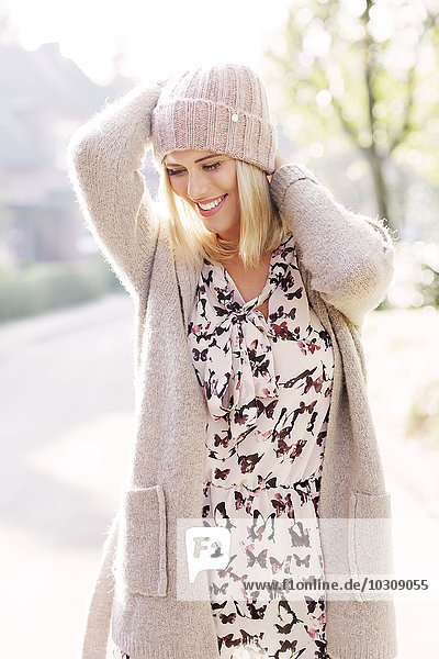 Lächelnde blonde Frau in gemustertem Kleid  Strickjacke und Wollmütze