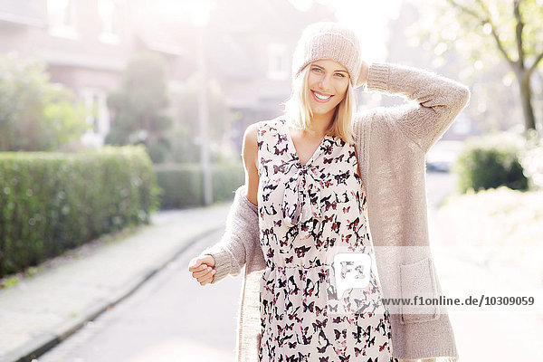 Porträt einer lächelnden blonden Frau in gemustertem Kleid  Strickjacke und Wollmütze