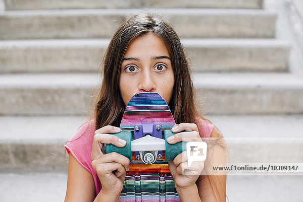 Portrait of wide-eyed teenage girl with a colorful skateboard sitting on stairs