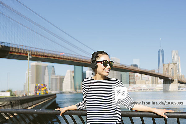USA  New York City  portrait of young woman hearing music with headphones in front of the skyline