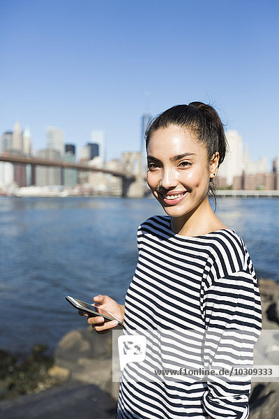 USA  New York City  Portrait einer lächelnden jungen Frau mit Smartphone