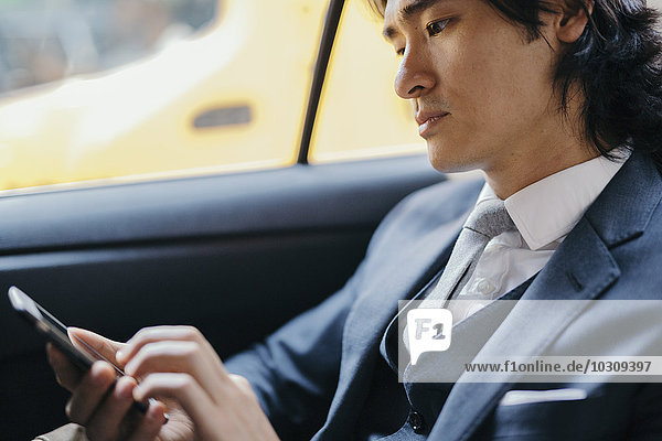 Businessman on back seat of car using cell phone
