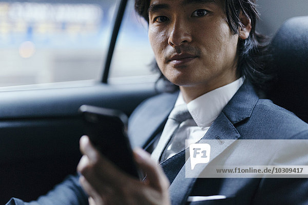 Portrait eines Geschäftsmannes auf dem Rücksitz eines Autos mit Handy