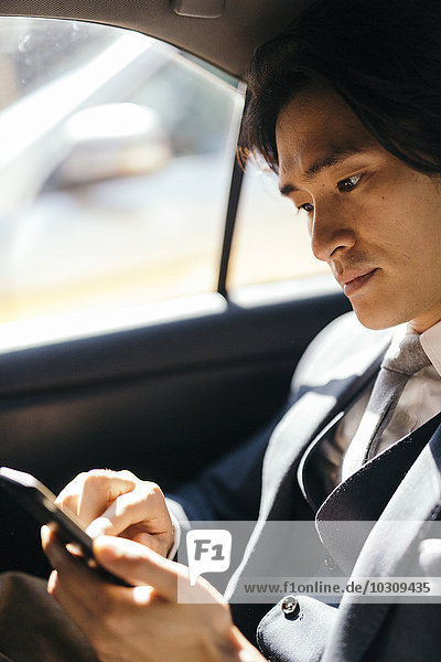Businessman on back seat of car using cell phone