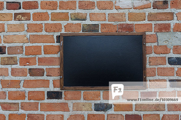 Blank blackboard hanging on brick wall
