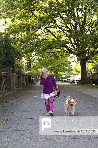 Porträt eines lachenden kleinen Mädchens  das mit seinem Hund spazieren geht.