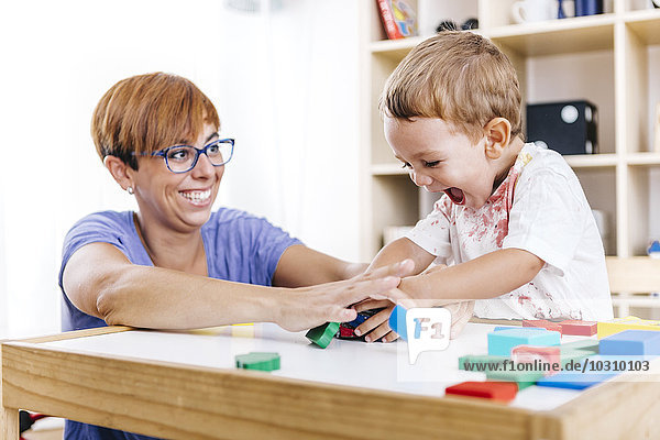 Portrait of little boy and his mother playing together with building bricks
