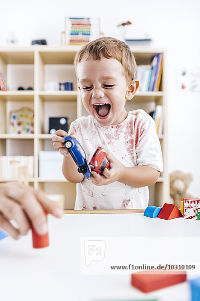 Porträt des lachenden kleinen Jungen beim Spielen mit Spielzeugautos