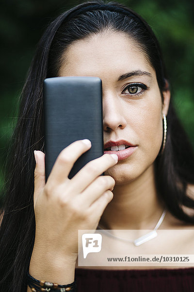 Junge Frau  die ein Auge mit dem Smartphone abdeckt