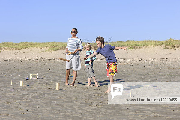 Mutter und ihre beiden Söhne spielen Kubb am Strand.