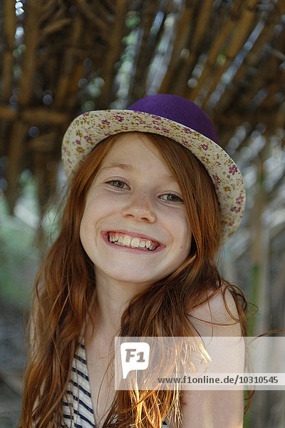 Porträt des grinsenden rothaarigen Mädchens mit Hut