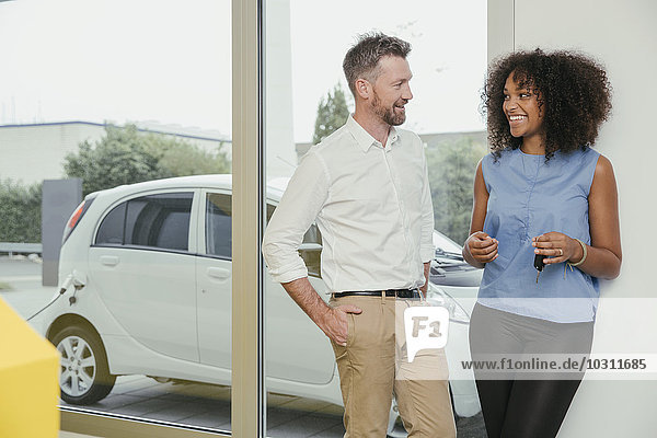 Man and woman talking while charging electric car  woman holding key