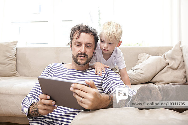 Der Mann und sein kleiner Sohn entspannen sich mit einem digitalen Tablett im Wohnzimmer.