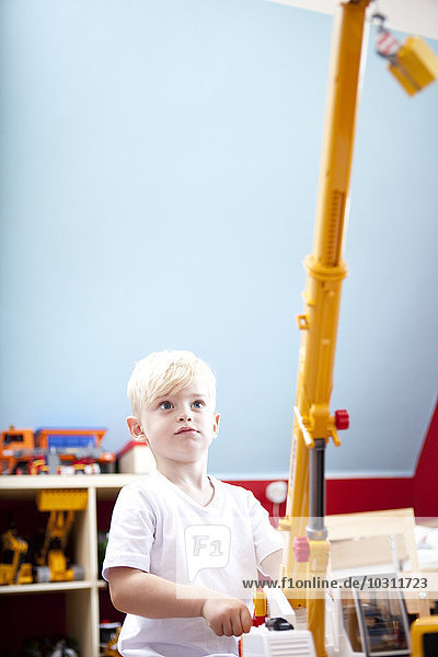 Kleiner Junge spielt mit Spielzeugkran im Kinderzimmer