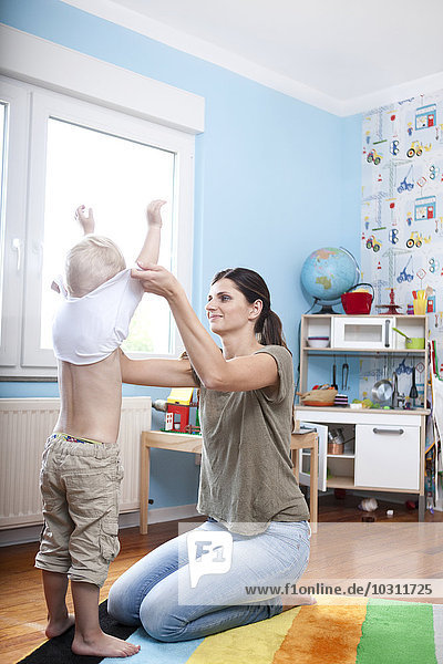 Frau beim Ausziehen seines kleinen Sohnes im Kinderzimmer