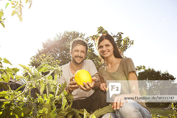 Smiling couple with yellow courgette in the garden