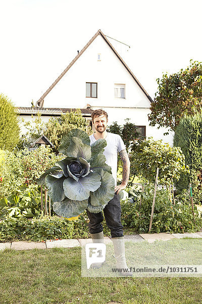 Portrait of man standing in the garden presenting red cabbage