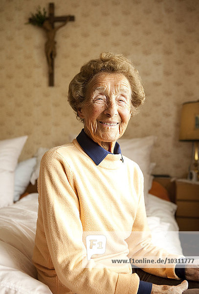 Portrait of aged woman sitting on bed at her bedroom