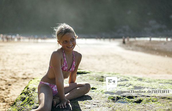 Portrait of a blond little girl sitting on a rock on the beach