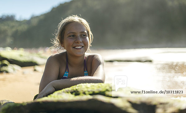 Porträt eines lächelnden Mädchens  das sich auf einen Felsen am Strand stützt.