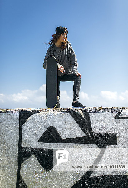 Porträt eines jungen Skateboardfahrers mit Baseballkappe an der Wand