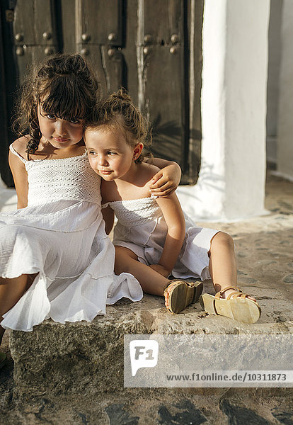 Spanien  Balearen  Menorca  Binibeca  Portrait von zwei kleinen Schwestern  die auf Stufen nebeneinander sitzen.