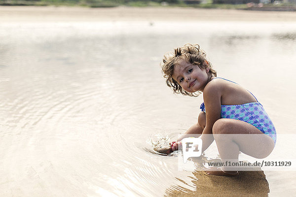Portrait of smiling little girl wearing swim suit playing at seafront