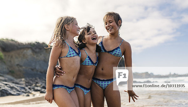 Spain  Colunga  three girls standing arm in arm on the beach having fun
