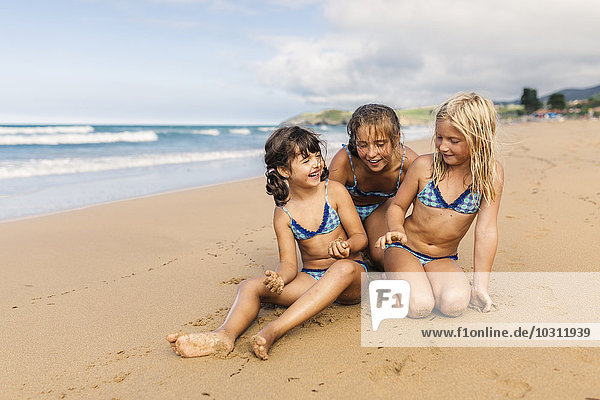 Spain  Colunga  three girls sitting on the beach having fun