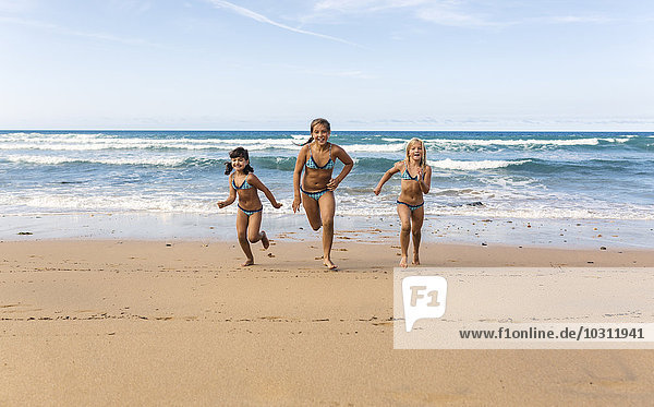 Spain  Colunga  three girls running side by side on the beach