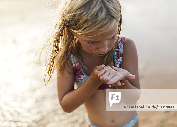 Kleines Mädchen am Strand mit einem Aal an der Hand