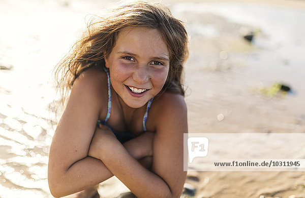 Porträt eines lächelnden Mädchens mit verschränkten Armen am Strand