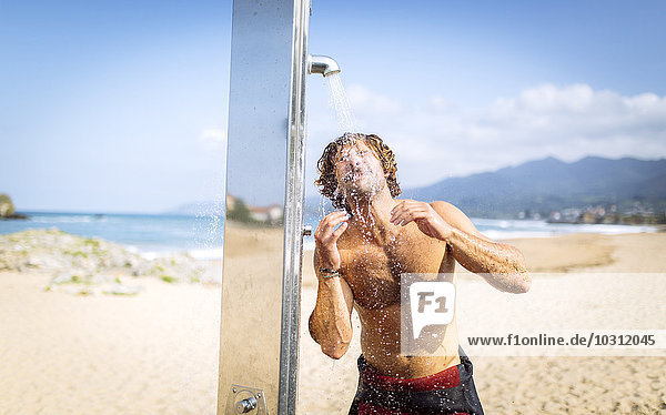Spain  Asturias  Colunga  young man on the beach taking a shower