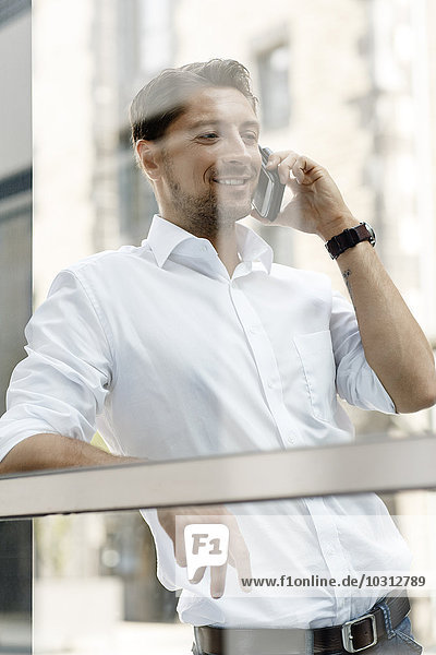 Geschäftsmann  der sich beim Telefonieren mit dem Smartphone an die Fensterscheibe lehnt