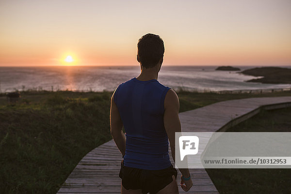 Spanien  Ferrol  Rückansicht eines Joggers  der auf einer Strandpromenade steht und den Sonnenuntergang beobachtet.